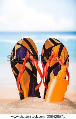 Slippers and sunblock in the sand background