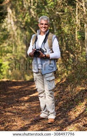 cheerful mid age man with dslr camera standing in forest