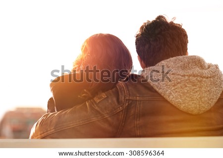 Closeup rear view of man embracing his woman while sitting on bench. They are sitting outdoor and looking away in a beautiful sunset light. Contemplative and aspirational mood.
 Royalty-Free Stock Photo #308596364