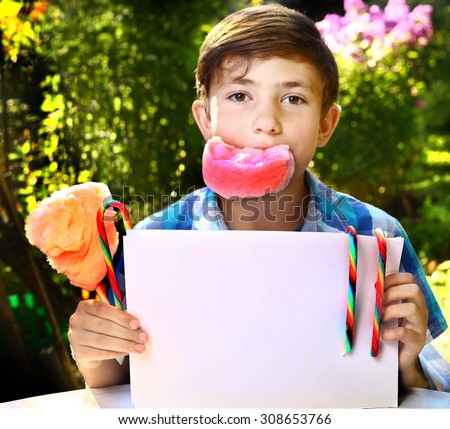 preteen handsome boy with cotton candy and sheet of paper on the summer garden background