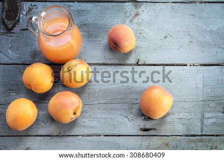 group of fresh apricots and juice in a glass jug on a rustic table from gray-blue wood, copy space