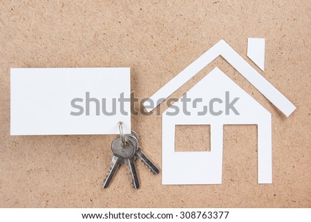 Silver key with house figure and blank business card on wooden background. Real Estate Concept. Top view.