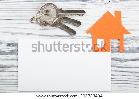 Silver key with house figure and blank business card on wooden background. Real Estate Concept. Top view.