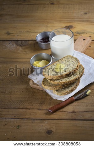 Freshly baked slice of whole grain bread loaf served with butter and jam and a glass of milk. Rustic wooden table top.