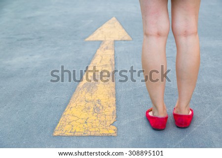 Girl wear red shoes  walking towards with yellow traffic arrow signage on an asphalt road background