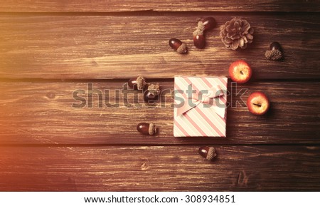 Gift box and pine cones with apples on wooden table.