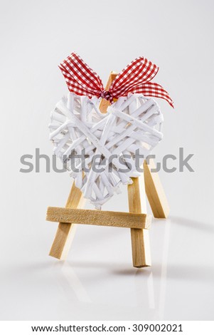 Little tripod wood easel with white raffia heart and red bow. 