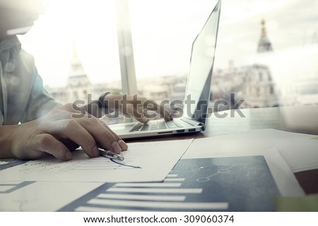 business documents on office table with laptop computer and graph financial diagram and man working in the background