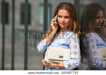 Middle-aged woman talking on mobile phone near office building. Pretty lady communicating with her friends or partners.