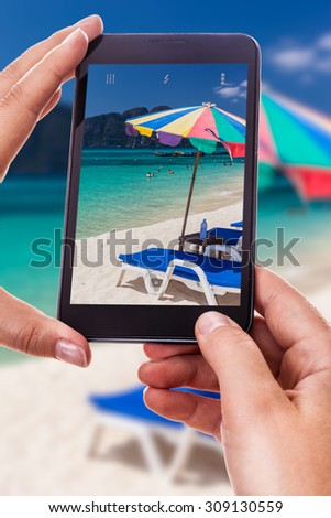 a woman using a smart phone to take a photo of a beautiful tropical beach