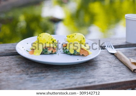 A plate with eggs benedict made with salmon and hollandaise sauce on a table by a pond in the park