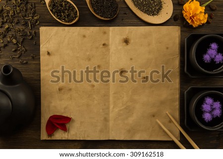 Black teapot, two cups, tea collection, flowers, old blank open book on wooden background. Menu, recipe, mock up