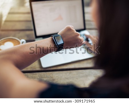 Close up shot of a woman checking time on her smartwatch. Female sitting in cafe with a laptop and cup of coffee. Royalty-Free Stock Photo #309171965