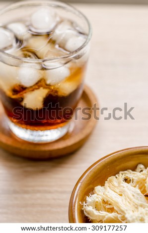 close up in dried squid and cola in glass on wooden background