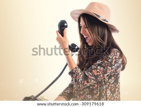 Angry woman talking to vintage phone  over ocher background