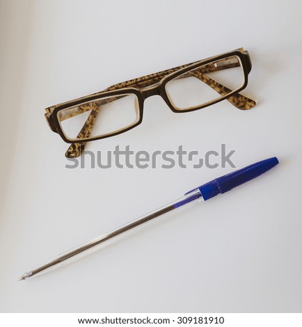 Old glasses and blue pen on the white office table