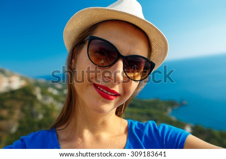 Girl in the hat making selfie by the smartphone on the background of sea coast,  Adriatic sea, Montenegro, Balkans