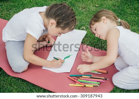 Children draw pictures with markers and pen on the grass in the park. Two creative girls paint horse from fairy tales