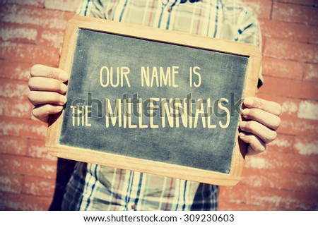 closeup of a young man holding a chalkboard with text our name is the millennials in front of a brick wall, slight vignette added  Royalty-Free Stock Photo #309230603
