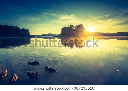 Vintage photo of beautiful sunset over calm lake. Landscape photographed in Mazury lake district.