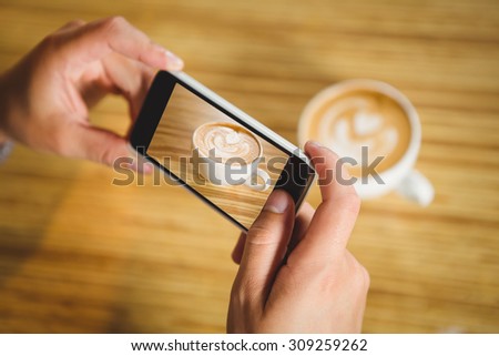Man photographing his cappuccino with coffee art at coffee shop
