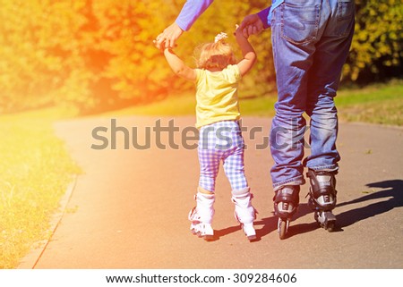 father teaching little daugther to roller skate in summer park