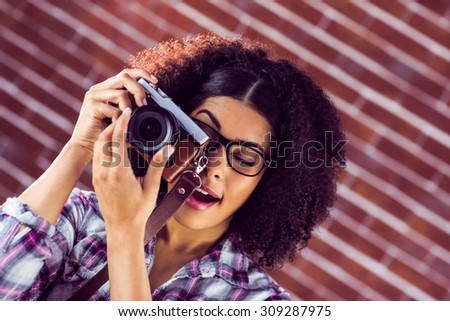 Attractive hipster photographing with camera against red brick background