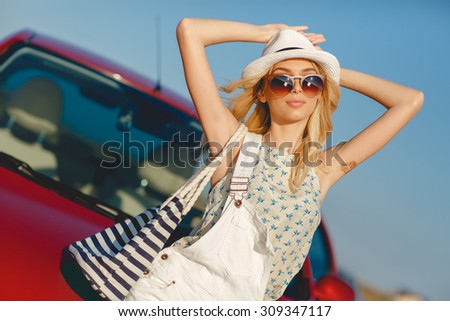 Summer vacation. Car trip. Travelling. Car travel. By the sea. Beautiful blonde woman standing with red small car on the background. Sea style. Summer vacation car road trip freedom concept. 