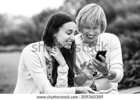 Mother with her daughter using phone dressed in yellow in the park. Black and white photo