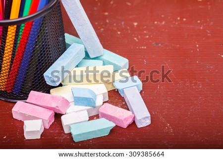 Heap of colorful pieces of chalk pastel pink violet green blue yellow white colors lying near office cup with pencils on old brown school table copyspace, horizontal picture