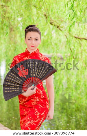 young Asian girl walking in national dress with a fan near the river