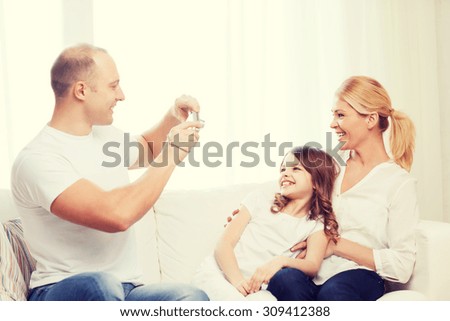 family, child, photography and home concept - smiling happy father taking picture of mother and daughter