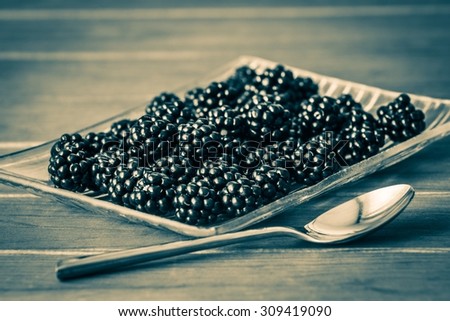glass plate with blackberries and spoon on wooden background