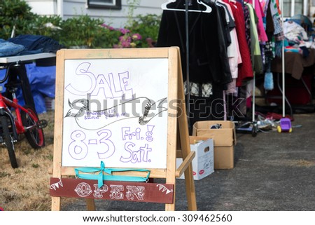 A hand-lettered sign advertises a home garage sale of used items.