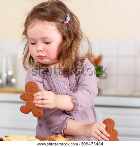 Happy little child, cute kid girl, sitting at the table in domestic kitchen making delicious sweet gingerbread xmas cookies. Kitchen decorated for Christmas