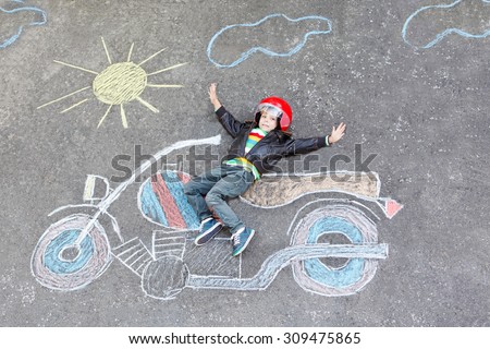 Creative leisure for children: Happy little child of four years in helmet having fun with motorcycle picture drawing with colorful chalks. Children, lifestyle, fun concept.