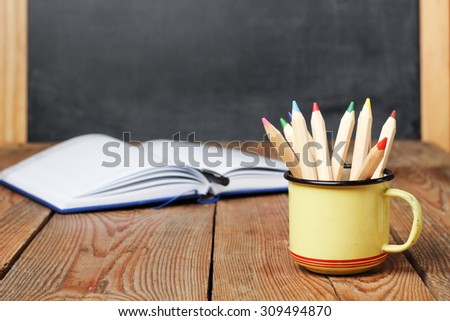 Still life, business, education concept. Pencils in a mug and open notebook on a wooden table with chalkboard. Selective focus, copy space, school background