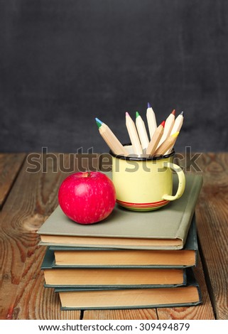 Still life, business, education concept. Pencils in a mug, books and apple on a wooden table with chalkboard. Selective focus, copy space, school background