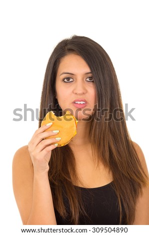 Hispanic brunette model wearing black top eating hamburger looking at camera, white background.