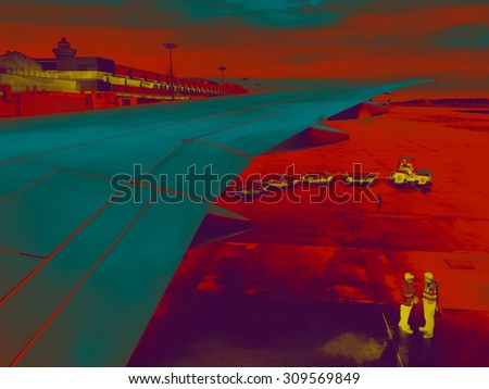 Airport staff at work under airplane wing on a runway, luggage cart coming - night vision or thermovision effect
