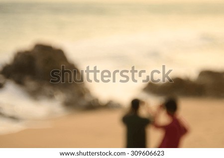 Blur man and woman taking photo with smart phone on tropical sunset beach abstract background.