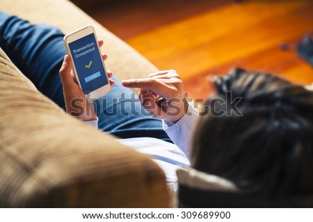 Woman using on line banking on mobile phone while lying down at home. Blue screen. Royalty-Free Stock Photo #309689900