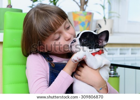 child girl kisses small pet a French Bulldog puppy 