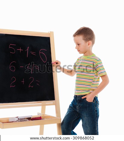chalkboard with math examples and a  firstgrader boy standing nearby