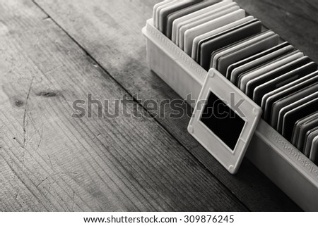black and white close up image of old slides frames and old camera over wooden table.
