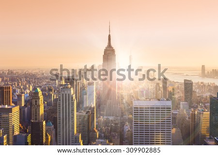 New York City. Manhattan downtown skyline with illuminated Empire State Building and skyscrapers at sunset. Horizontal composition. Warm evening colors. Sunbeams and lens flare.