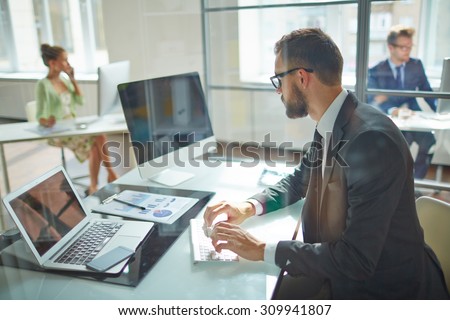 Young employee looking at computer monitor during working day in office Royalty-Free Stock Photo #309941807