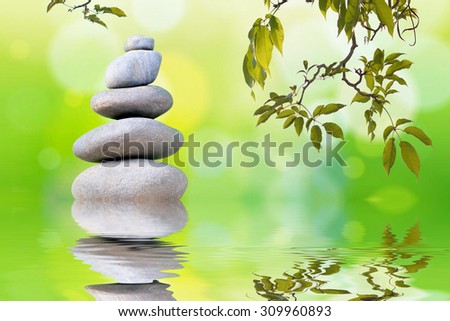 Pyramid of the stones isolated and tree branches with green leaf or Zen pebbles balance on green bokeh background. Spa Concept.