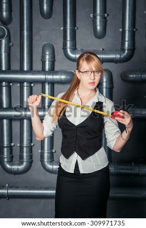 Attractive businesswoman wearing glases holding measure tape on PVC pipes background
