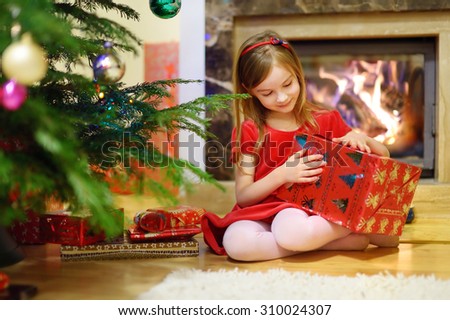 Adorable little girl opening Christmas gifts by a Christmas tree in cozy living room